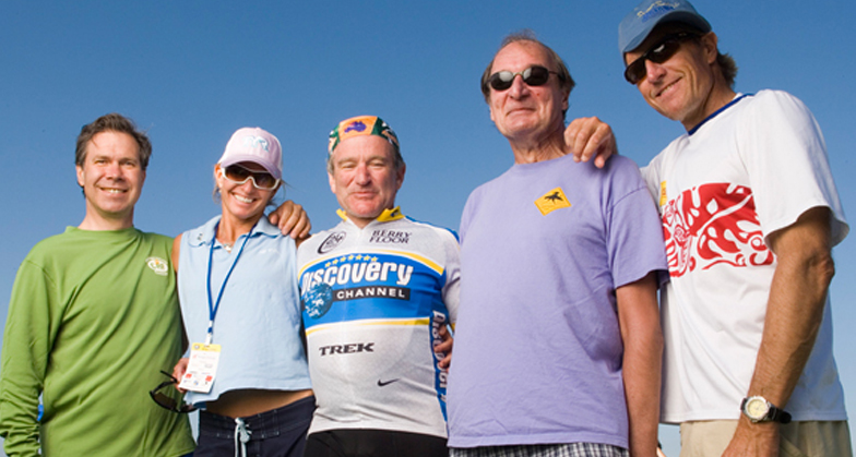 Robin Williams in a Discovery Channel cycling jersey stands with fellow athletes and supporters smiling at the San Diego Triathlon Challenge.