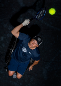 David Wagner sitting in wheelchair with tennis ball and swinging racquet