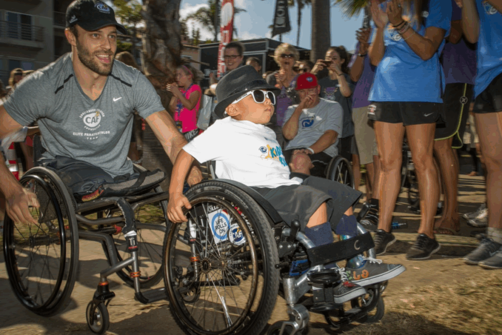 Andre Kajlich pushing a young boy in a wheelchair during a CAF event, surrounded by cheering supporters