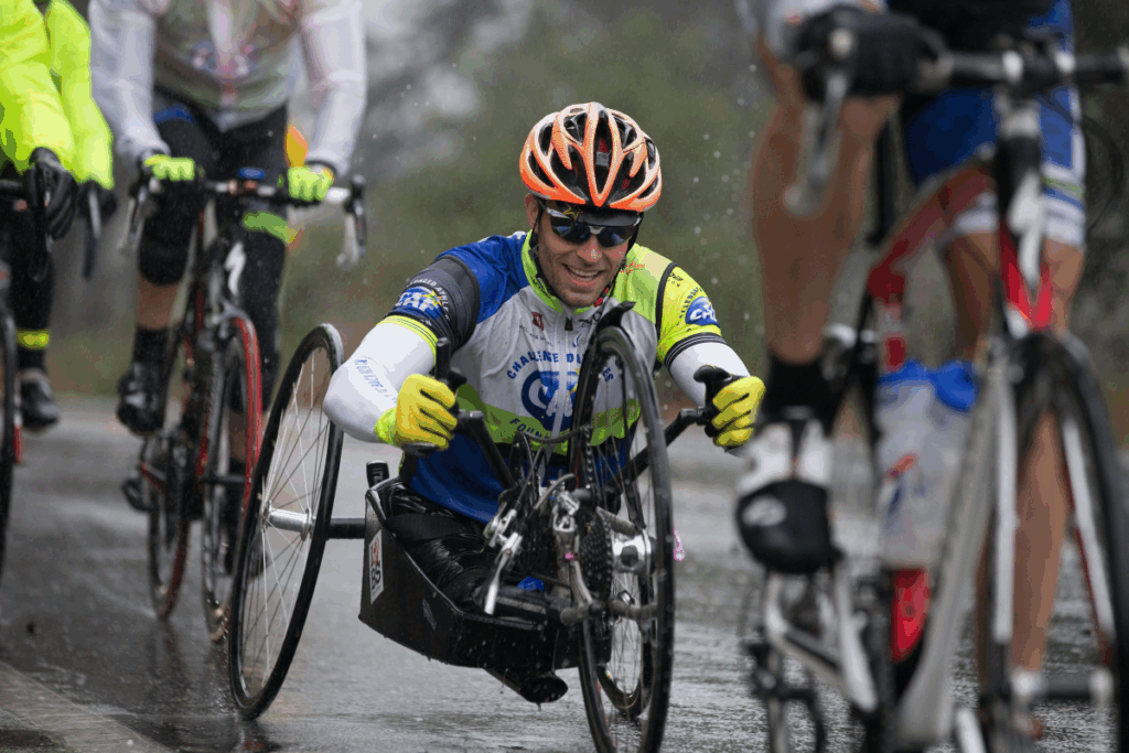 Andre Kajlich smiling while competing in a handcycle during a rainy group ride with cyclists