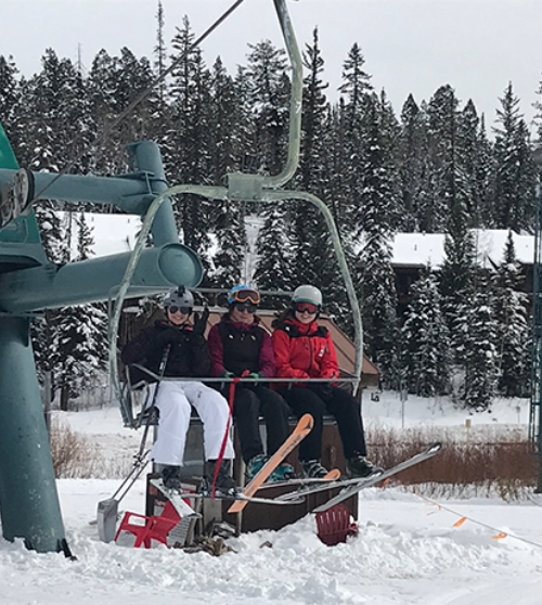 Three skiers ride a chairlift surrounded by snow-covered trees at a mountain resort.