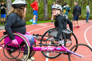 Two girls in wheelchair race chairs on track