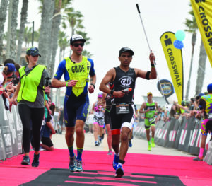 Adrian Broca visually impaired triathlete crossing finish line at IRONMAN 70.3 Oceanside