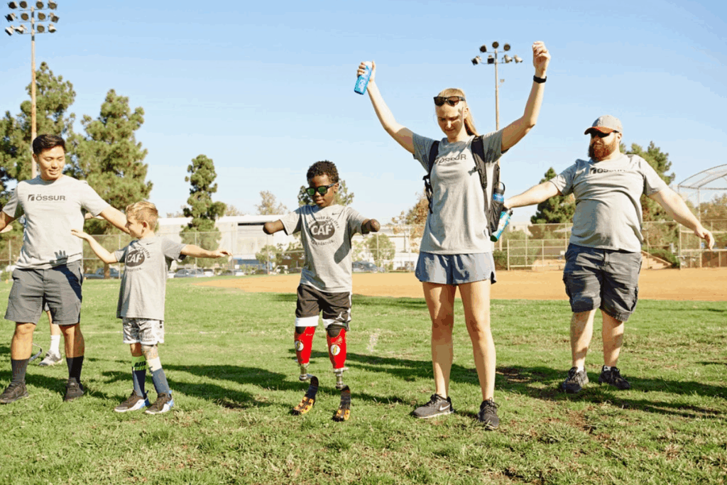Young athletes with prosthetics and adults stretch their arms in a warm-up line at a CAF mobility clinic.