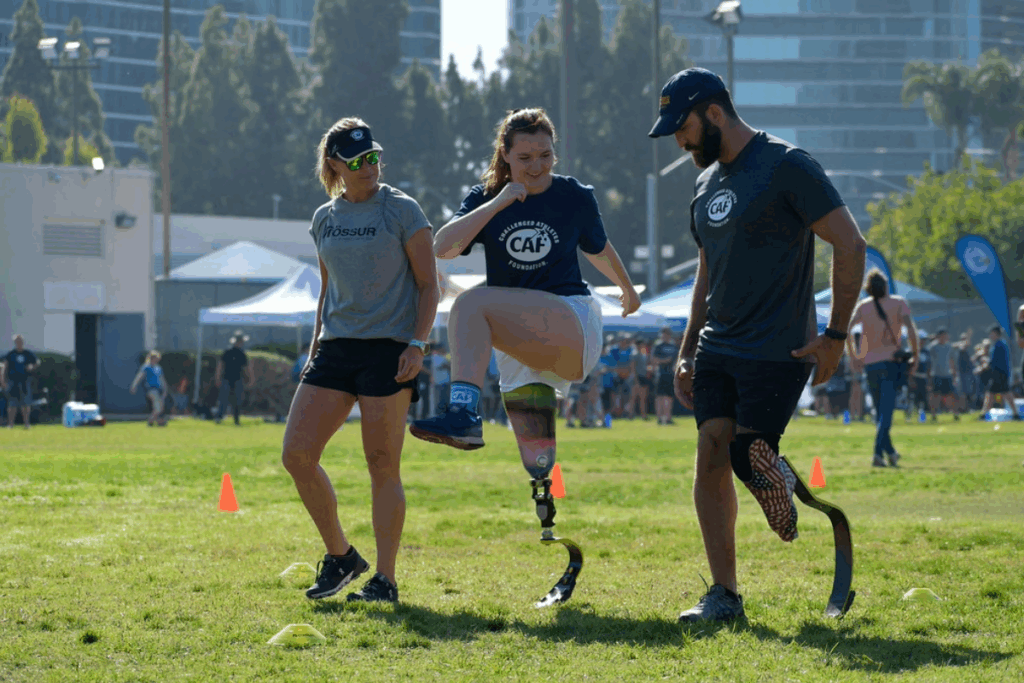 A young athlete with a running blade practices high knees between two coaches during a CAF mobility clinic.