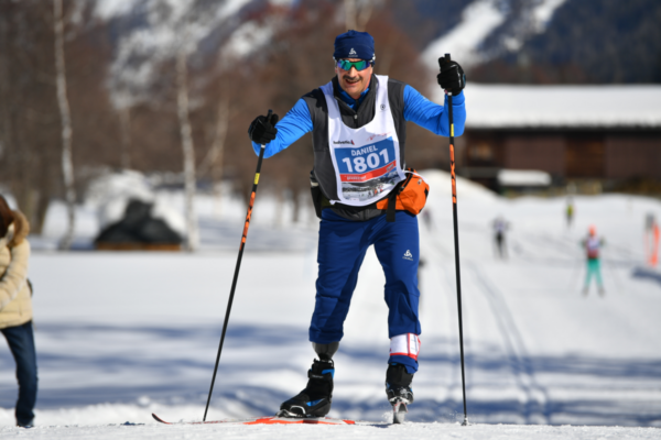 An athlete with a physical disability competes in a Nordic ski race, wearing a bib and using ski poles while gliding along a snow-covered course.