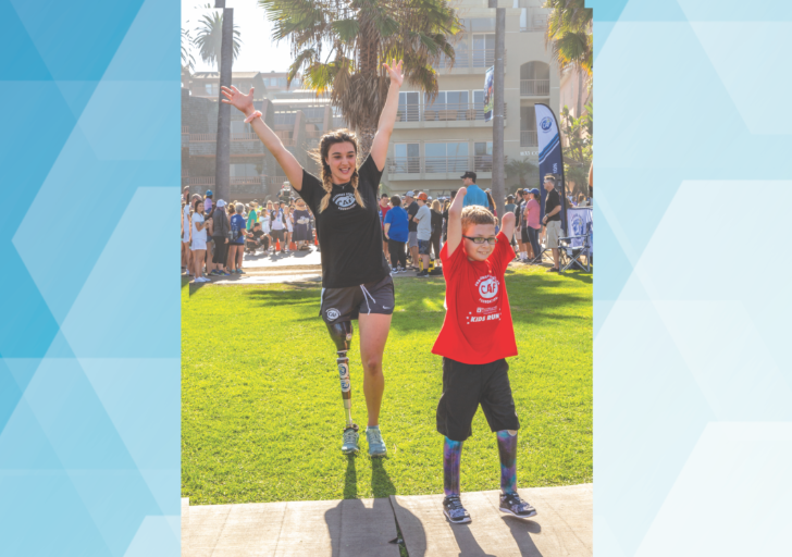 An athlete with a physical disability wearing a prosthetic leg and a young participant stand side by side on a grassy lawn with their arms raised, smiling as they celebrate together at an outdoor CAF event with palm trees and a crowd in the background.