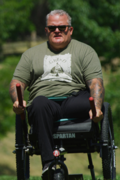 An athlete with a physical disability uses a GRIT Freedom Chair outdoors, gripping the hand levers while seated upright on a grassy field.