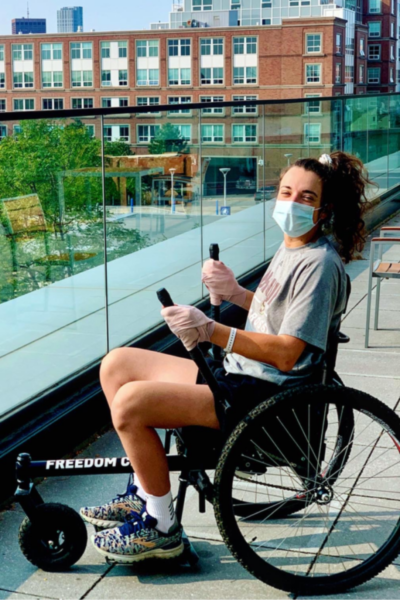 An athlete with a physical disability wears a face mask and gloves while using a GRIT Freedom Chair along an elevated outdoor walkway.