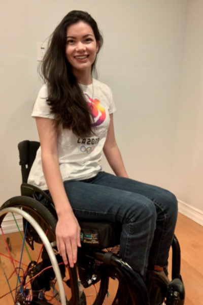 A CAF athlete with a physical disability smiles while seated in a wheelchair, wearing a Team USA shirt in an indoor setting.