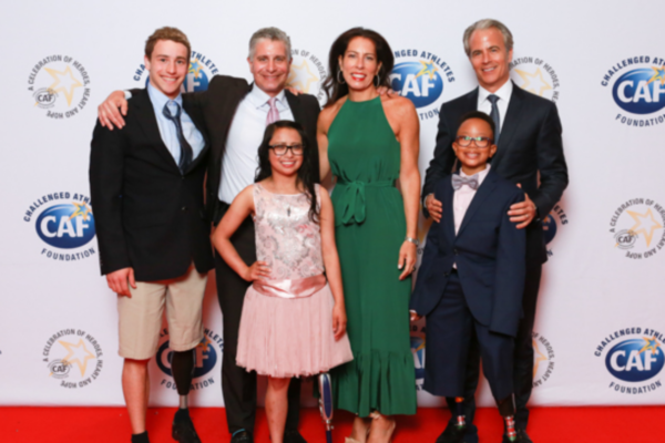 CAF athletes with physical disabilities and supporters pose together on the red carpet at Celebration of Heroes, smiling in formal attire in front of a Challenged Athletes Foundation step-and-repeat backdrop.