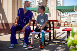 Lucas Cronan sitting with Prosthetist on table bench