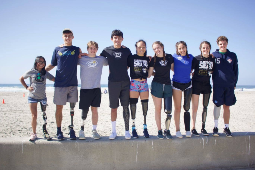Teen amputees pose side by side on boardwalk wall