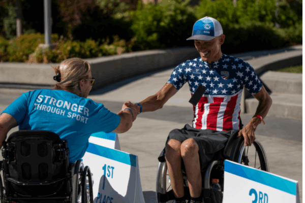 Two athletes in wheelchairs share a congratulatory handshake near the winner’s podium.
