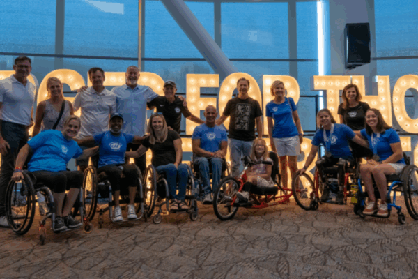 Group of CAF athletes, supporters, and volunteers gather for a photo indoors with glowing event signage.