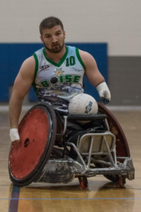 Kory Puderbaugh in rugby wheelchair playing rugby with ball in lap