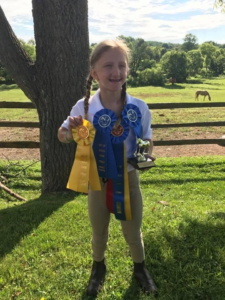 Young Sarah Oldenski standing in grass with ribbons and trophy