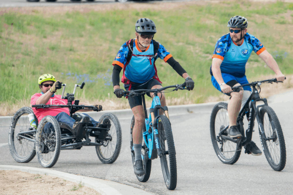 Three riders, including one using a handcycle, ride together on a paved path during an adaptive cycling event.