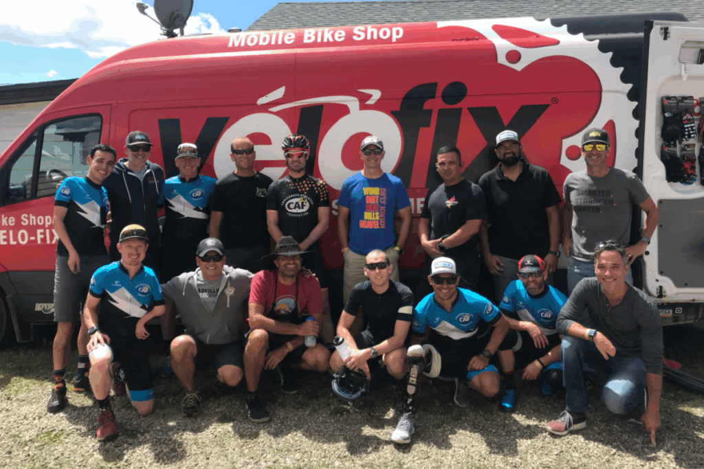 Cycling team and support crew pose for a group photo in front of a red Velofix mobile bike shop van.