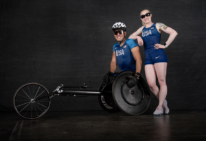 Erik Hightower in racing wheelchair with wife Kym Crosby standing beside him both in Team USA uniform