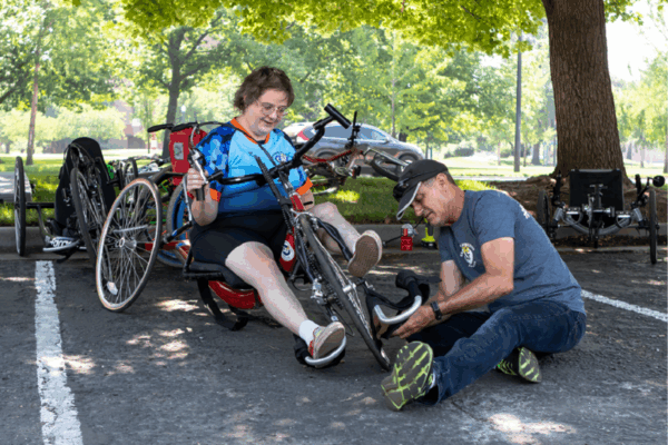 An athlete is being helped by a volunteer to fix their wheelon their accesible bike