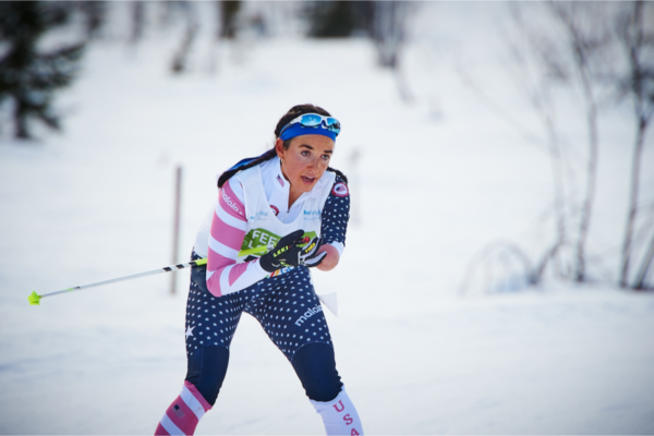 Athlete with a physical disability competes in adaptive Nordic skiing, leaning forward with intensity while pushing off ski poles on a snowy race course.