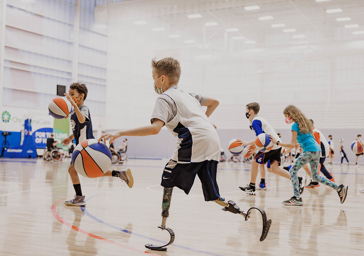 Youth athletes with physical disabilities practice dribbling during an indoor basketball drill, moving across the court with focus and energy.
