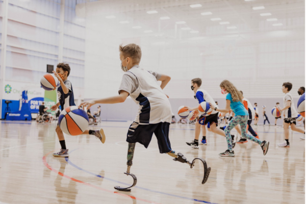 Youth athletes with physical disabilities practice dribbling during an indoor basketball drill, moving across the court with focus and energy.