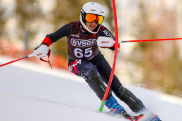 An athlete with a physical disability carves through a slalom gate on an alpine ski course, leaning into a turn during a competitive run.