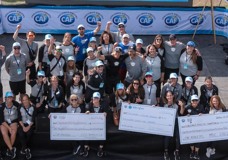CAF staff and volunteers celebrating together on stage, holding large fundraising checks at SDTC.