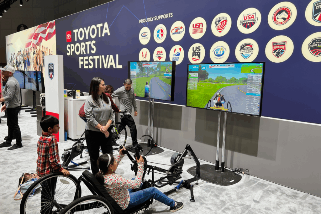 A child uses a handcycle on indoor bike trainers while watching a cycling simulation screen at the Toyota Sports Festival.