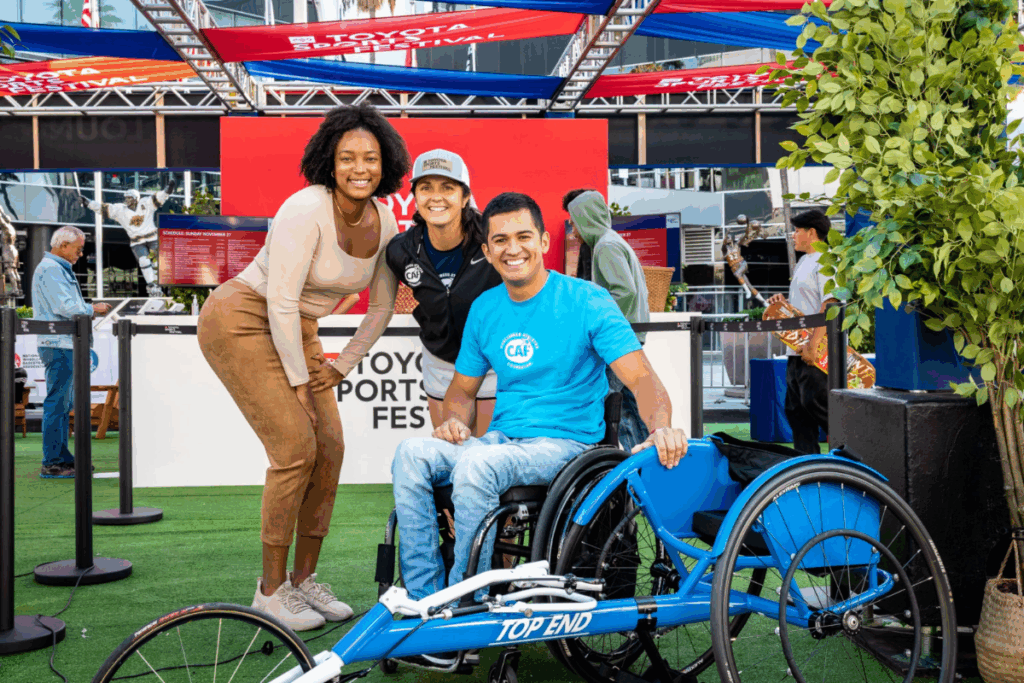 Three people smile for a photo with a racing wheelchair at the Toyota Sports Festival.