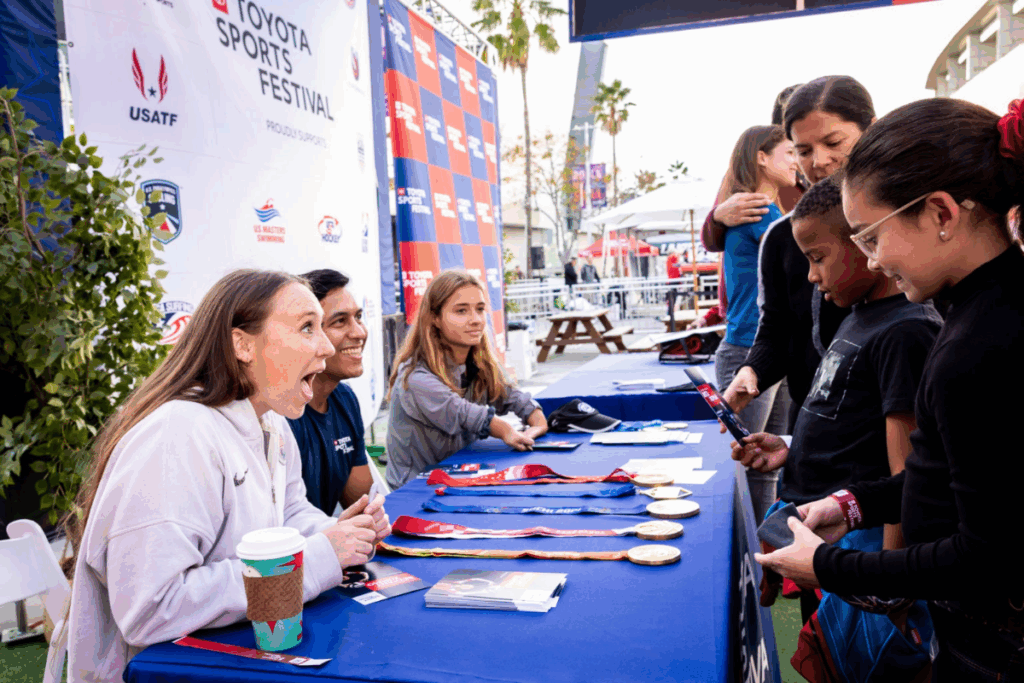 Paralympic athletes and medalists interact with children at a signing table displaying their medals at the Toyota Sports Festival.