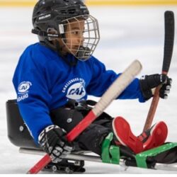 Young athlete plays sled hockey on the ice wearing a blue CAF Idaho jersey.