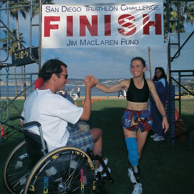 Athlete Jim Maclaren using a wheelchair high-fives a runner with a prosthetic leg at the San Diego Triathlon Challenge finish line.