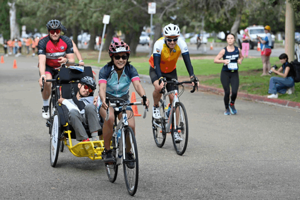 A cyclist pulls an adaptive athlete in a yellow race chair attached to her bike, accompanied by two other cyclists, during the cycling portion of the CAF challenge.