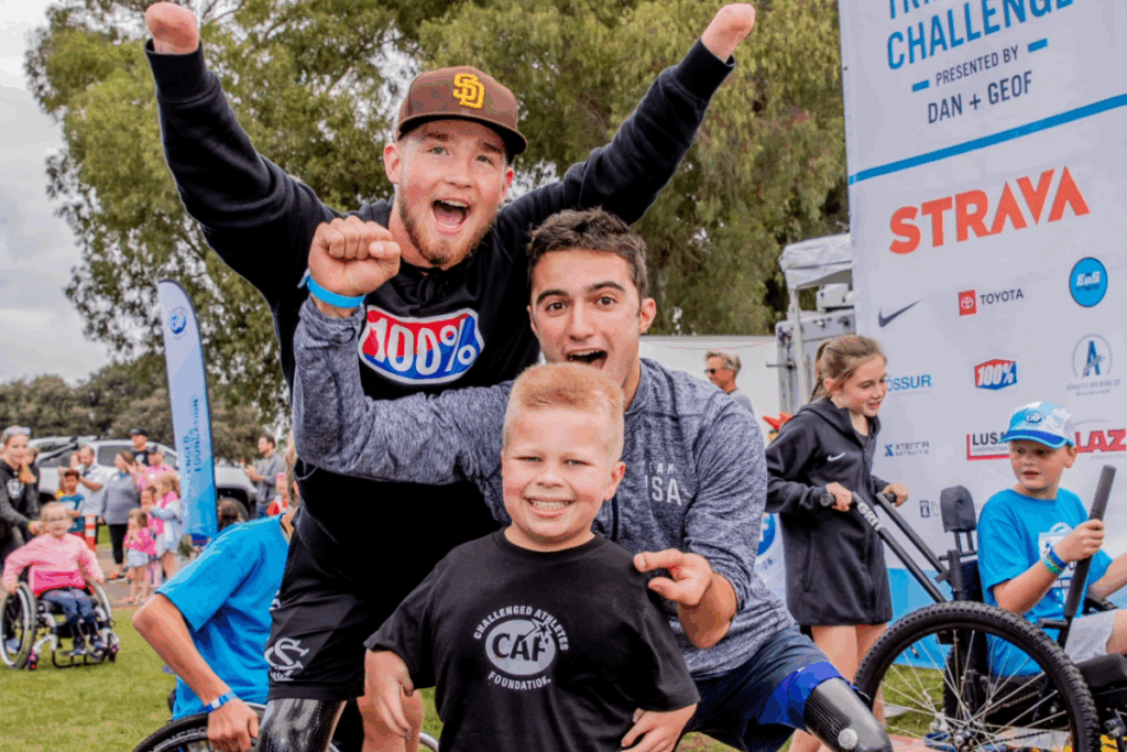 Two enthusiastic athletes pose with a young boy in a CAF shirt, all smiling and cheering at the finish area surrounded by other participants and families.