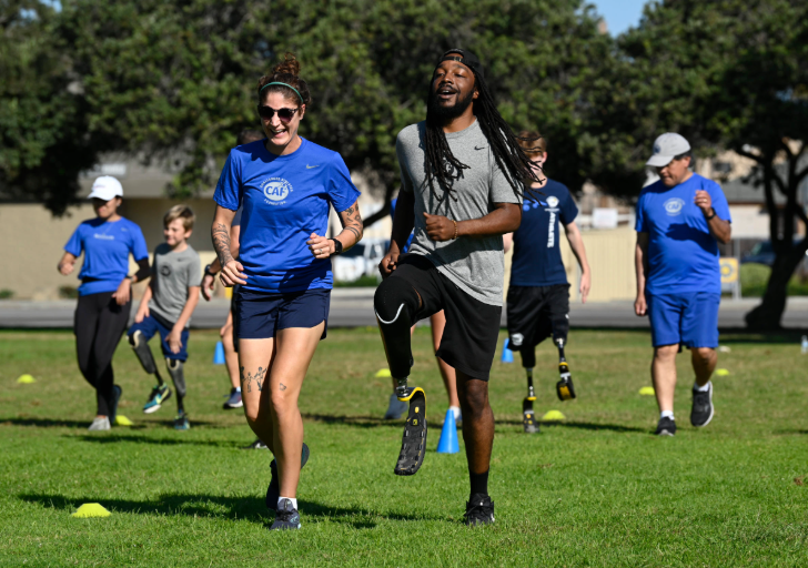 A group of athletes, including amputees with running blades, jogging together on a sunny field during a CAF training session.