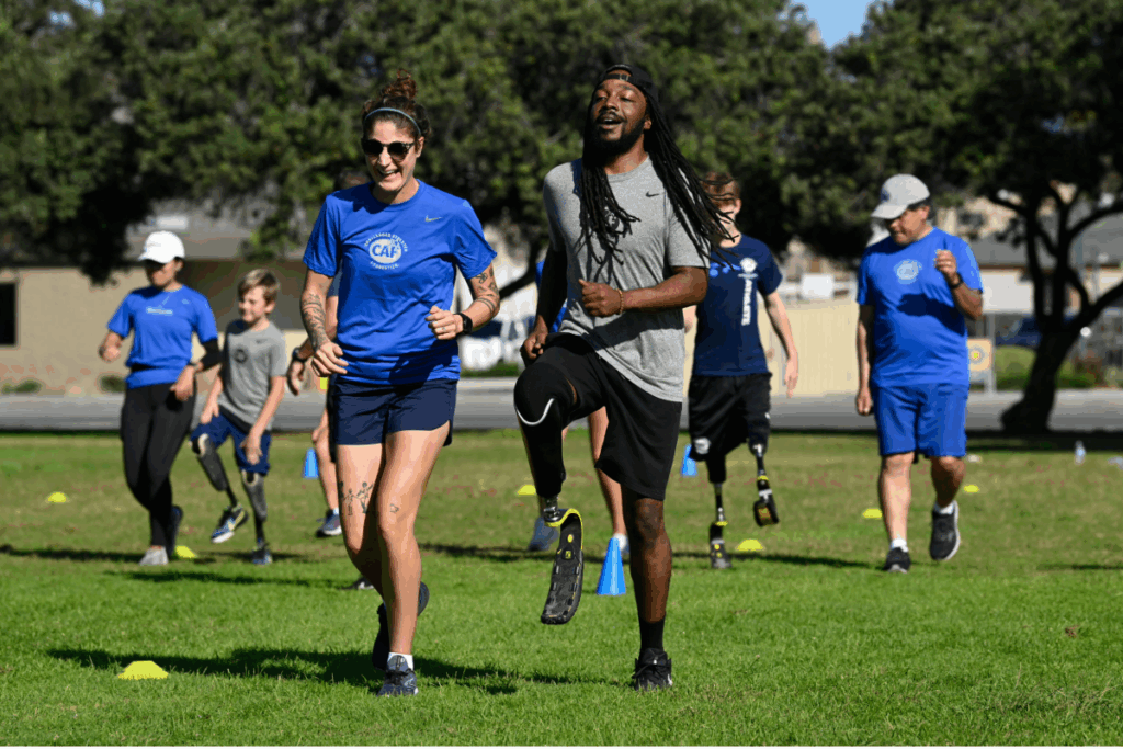 A group of athletes, including amputees with running blades, jogging together on a sunny field during a CAF training session.