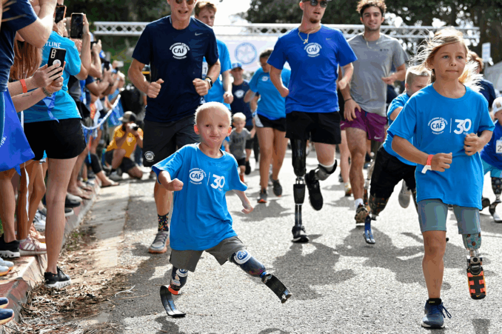 Young children, including several with prosthetic running blades, sprinting joyfully down a crowded street lined with cheering spectators.