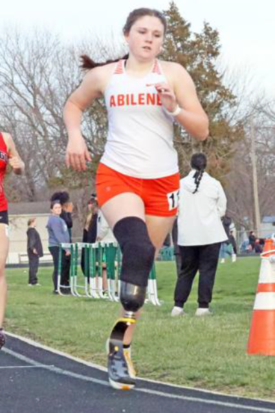 A high school track athlete with a prosthetic running blade competes in a race wearing an Abilene team uniform.