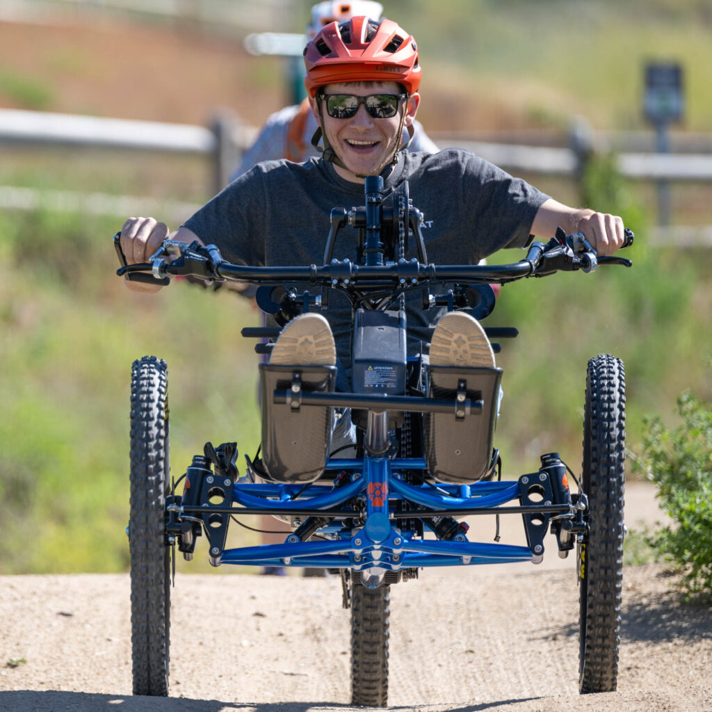 A person smiling wide while riding an adaptive mountain bike on trails.