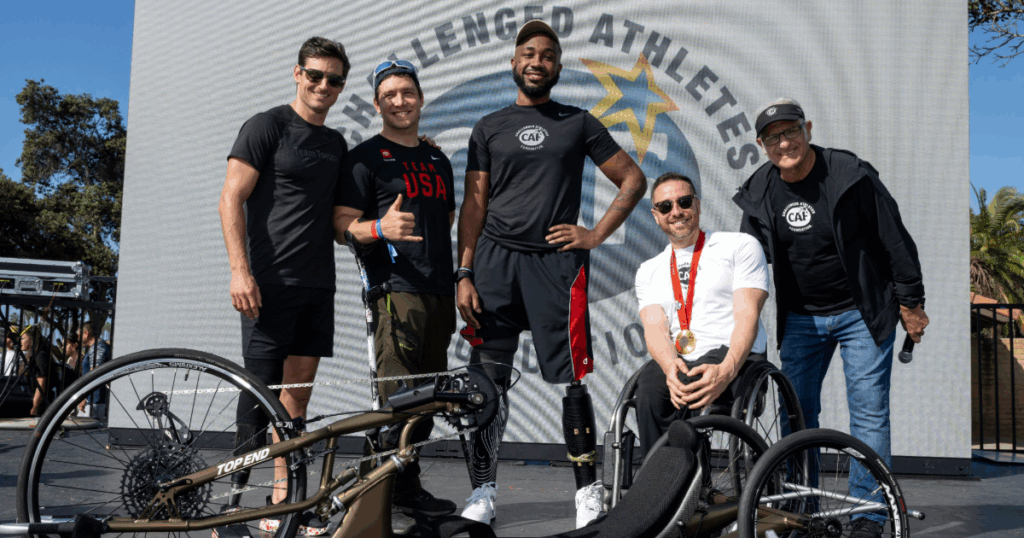 Adult athlete Akeem Kearse receiving a CAF grant on stage at the san diego triathlon challenge smiling in a group together