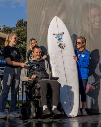 Athlete Collin Bosse with a physical disability in a wheelchair receiving a CAF grant for a surf board on stage at the san diego triathlon challenge