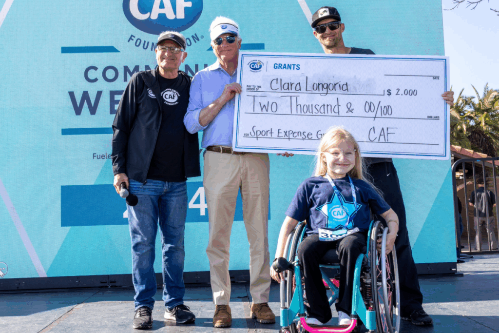 Youth athlete Clara Longoria receiving a sports expense grant smiling on stage at the san diego triathlon challenge