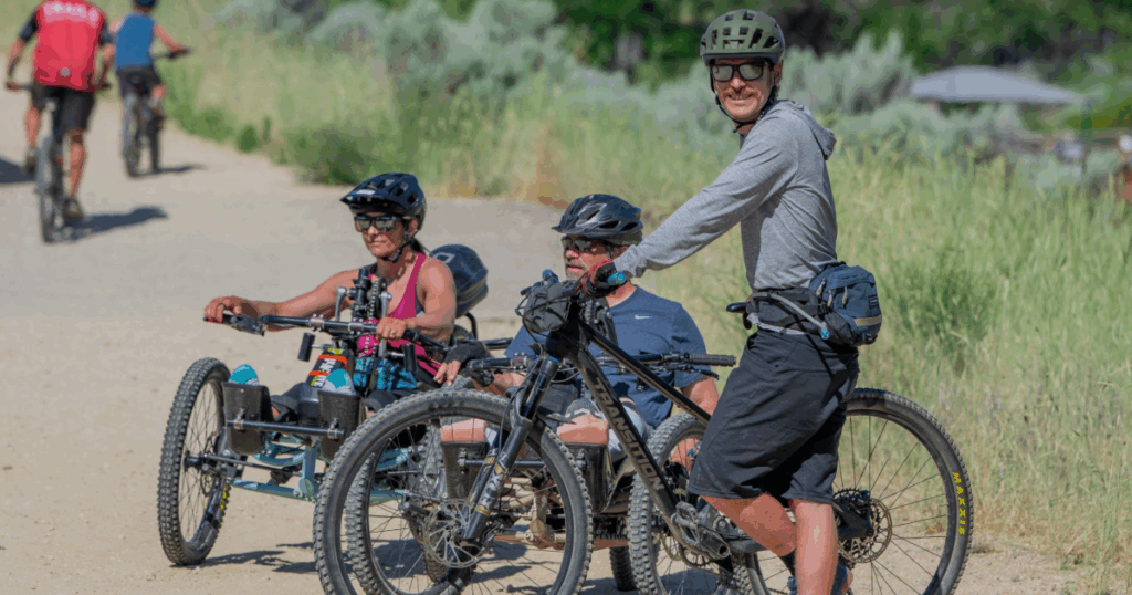 Two athletes on adaptive mountain bikes and a cyclist taking a break on the trail during CAF Idaho Mountain Bike Weekend
