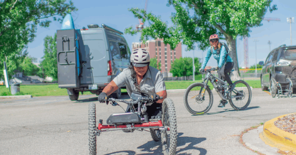 Athlete using an adaptive mountain bike practicing on pavement with a cyclist riding nearby
