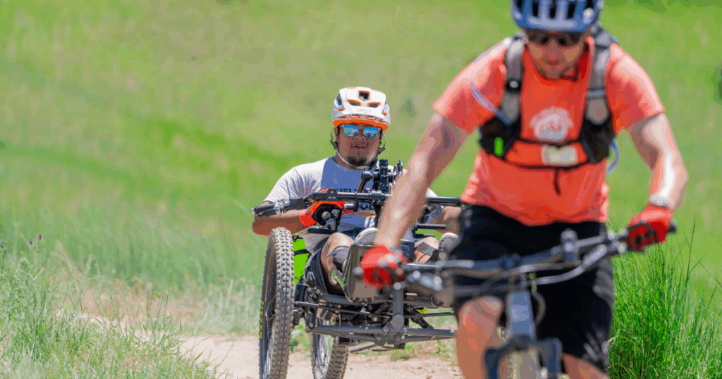Athlete using an adaptive mountain bike riding a dirt trail alongside a cyclist at CAF Idaho Mountain Bike Weekend