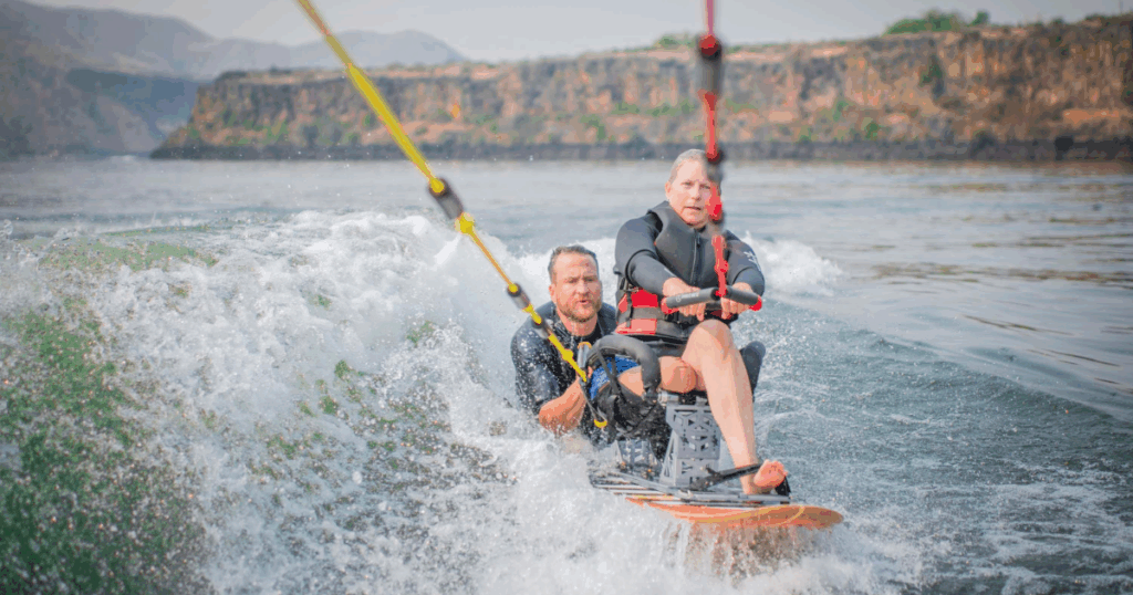 Athlete with physical disability waterskiing with support, riding waves during CAF Idaho Water Sports Weekend.