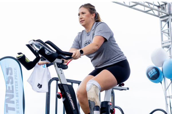 Adaptive athlete with a lower-limb prosthesis rides a stationary bike during a fitness event, demonstrating strength, training, and active living.